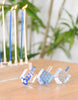 Load image into Gallery viewer, This is a lifestyle picture of the acrylic Hanukkah dreidels. The three dreidels are arranged on top of a wooden table, with part of an acrylic Menorah visible in the background, having its candles lit.
