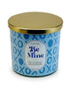 Load image into Gallery viewer, Front angle of the Valentine scented candle. In this view, all the features of the candle can be fully appreciated: The sky blue container adorned with a blue-colored pattern of the term &quot;XOXO,&quot; the white label displaying the term &quot;Be Mine&quot; and its ingredients; and the golden lid atop the jar. The background of the picture is white.

