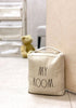 Load image into Gallery viewer, Lifestyle picture of the decorative door stopper. It is positioned against a cream-colored door, standing on a white floor. The background is blurry, but a teddy bear, half of an upholstered chair, and a three-tier white storage unit can be distinguished in the distance.
