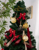 Load image into Gallery viewer, Second lifestyle picture of the set of four lighting up Christmas ornaments. They are placed together on a high part of a Christmas tree, right below the very top. The photo captures the tree from the middle to the highest part. Besides the ornaments, this Christmas tree is decorated with a red ribbon that wraps around the tree, a few red and gold Christmas balls, three red ribbons hanging on it, and an ornament on the top that states the phrase &quot;Merry Christmas.&quot;
