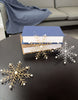 Load image into Gallery viewer, Lifestyle picture of the Christmas ornaments with snowflake shape. They are placed on a  dark brown circular table, in front of two books that are placed one above another.
