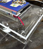 Load image into Gallery viewer, Second lifestyle picture of the acrylic table. It shows a close-up of a side of the tabletop, highlighting the clean clarity and sleekness of the table&#39;s acrylic material. Three stacked books can be seen resting on top.
