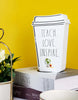 Load image into Gallery viewer, A lifestyle picture of the coffee-themed teacher décor. It is positioned at a frontal angle, slightly tilted to the right. The sign stands on a stack of two books: the upper one gray and the lower one purple. A yellow wall is visible behind the sign. In the frontal left part of the photo, a white vase with green plants can be seen.
