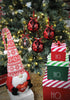 Load image into Gallery viewer, Lifestyle picture showcasing the gnome-themed Christmas tree balls. They are hanging on a Christmas tree with lighting bulbs on it. In front of the tree, there&#39;s a red and white Christmas gnome that holds a red decorative heart. There are also three decorative red, white, and green Christmas boxes on the right side, one above the other.
