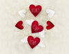 Load image into Gallery viewer, Lifestyle picture of the Valentine garland with hearts. The picture presents the garland in a close look. The item is rolled up, placed on an off-white faux fur tablecloth. The close-up photo allows full appreciation of the terms &quot;XOXO&quot; and &quot;Love&quot; on the hearts.
