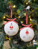 Load image into Gallery viewer, Lifestyle picture of these Santa and Mrs. Claus ornaments. They are hanging on a Christmas tree with lighting bulbs on it. The light is reflected on the ornaments, giving it a shining effect.

