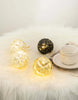 Load image into Gallery viewer, Lifestyle picture of this set of four ornaments that light up. They are on a table with a white plush tablecloth, illuminating the surroundings with their lights.
