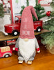 Load image into Gallery viewer, Lifestyle picture of the skiing Christmas gnome. It is placed on a wooden table, with a few Christmas decorations around it. The most noticeable is a red decorative truck behind it; the truck is carrying a mini Christmas tree.
