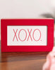 Load image into Gallery viewer, Lifestyle picture of the Valentine-themed sign positioned at a frontal angle. The sign is placed on a dark wooden tabletop. In the far background of the picture, a white-colored wall can be appreciated in a blurred view.
